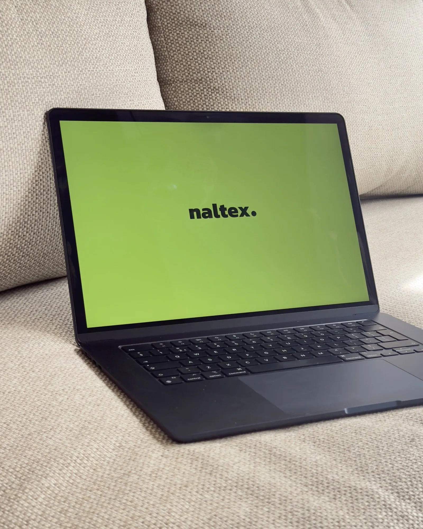 De MacBook van Naltex met de Naltex-wallpaper op de bank in het tuinhuis