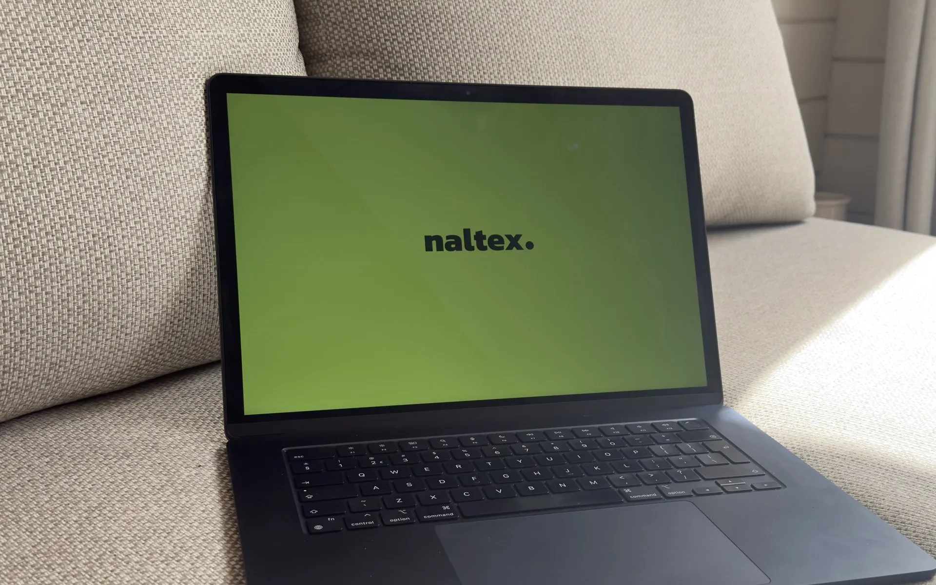 De MacBook van Naltex met de Naltex-wallpaper op de bank in het tuinhuis
